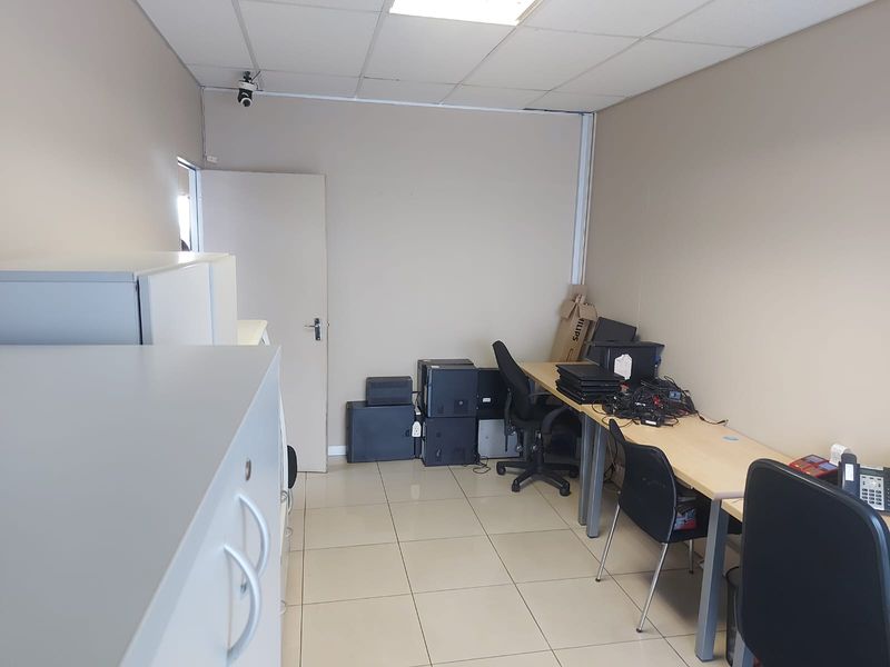 A functional office space featuring ceramic floor tiles, a suspended ceiling, and integrated security camera, suitable for a professional work environment.