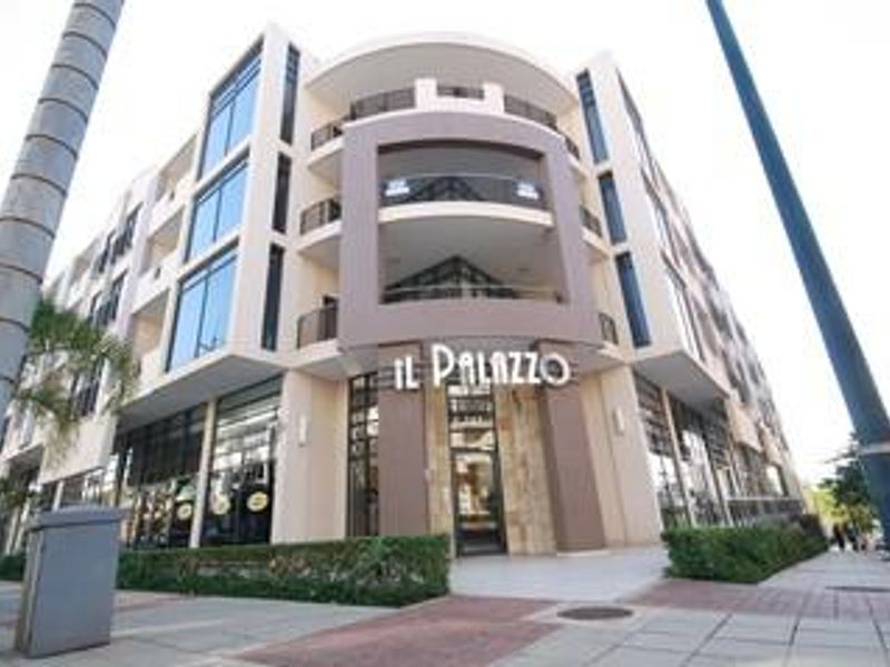 A modern multi-story office building facade featuring glass windows, stone accents, and integrated balconies at the street level entrance.