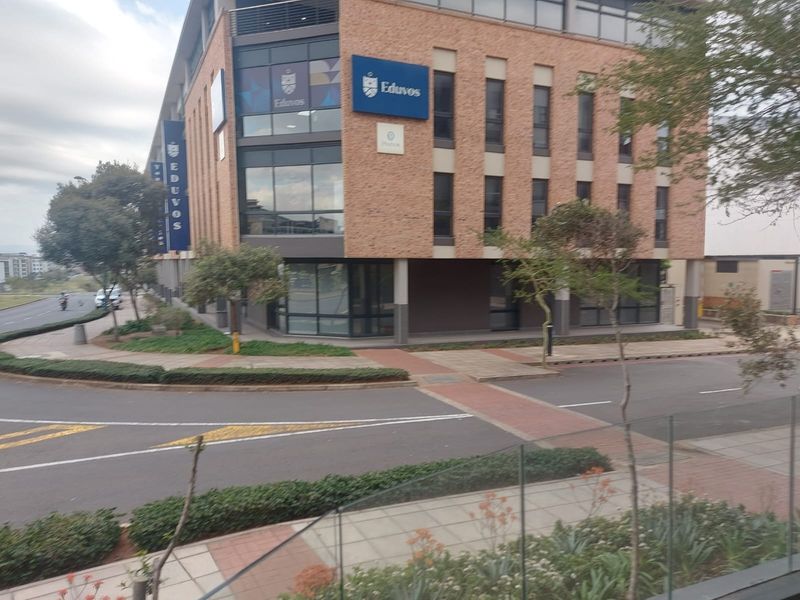 Exterior view of a modern multi-story commercial building featuring brick and glass facade elements, situated on a corner lot with paved pedestrian access.