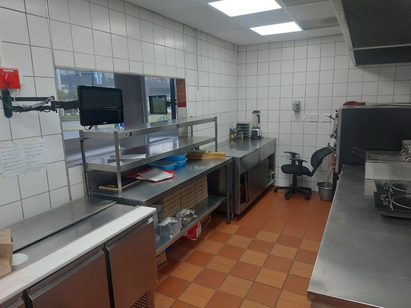 Commercial kitchen space featuring stainless steel prep surfaces, tiled walls, and industrial-grade flooring, suitable for food preparation and service operations.