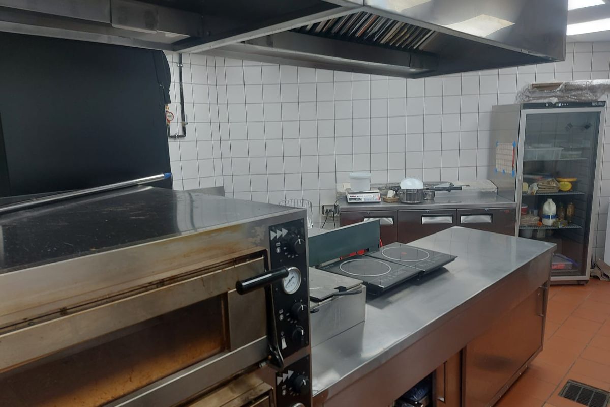 Commercial kitchen space featuring stainless steel prep counters, a large oven, professional extractor hood, and tiled wall finishes.