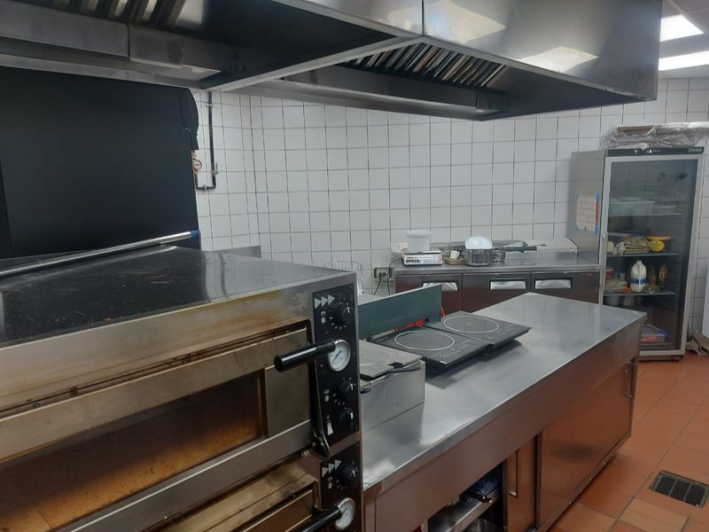 Commercial kitchen space featuring stainless steel prep counters, a large oven, professional extractor hood, and tiled wall finishes.