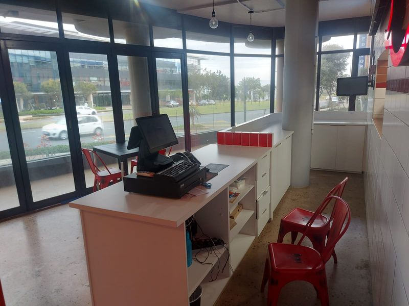 A bright open-plan retail space featuring floor-to-ceiling windows, a built-in service counter, and modern tiled wall finishes.