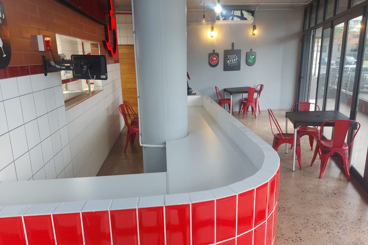 Modern retail space featuring a vibrant red tiled service counter, polished concrete floors, and large glass windows providing ample natural light.