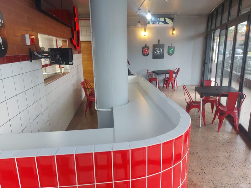 Modern retail space featuring a vibrant red tiled service counter, polished concrete floors, and large glass windows providing ample natural light.