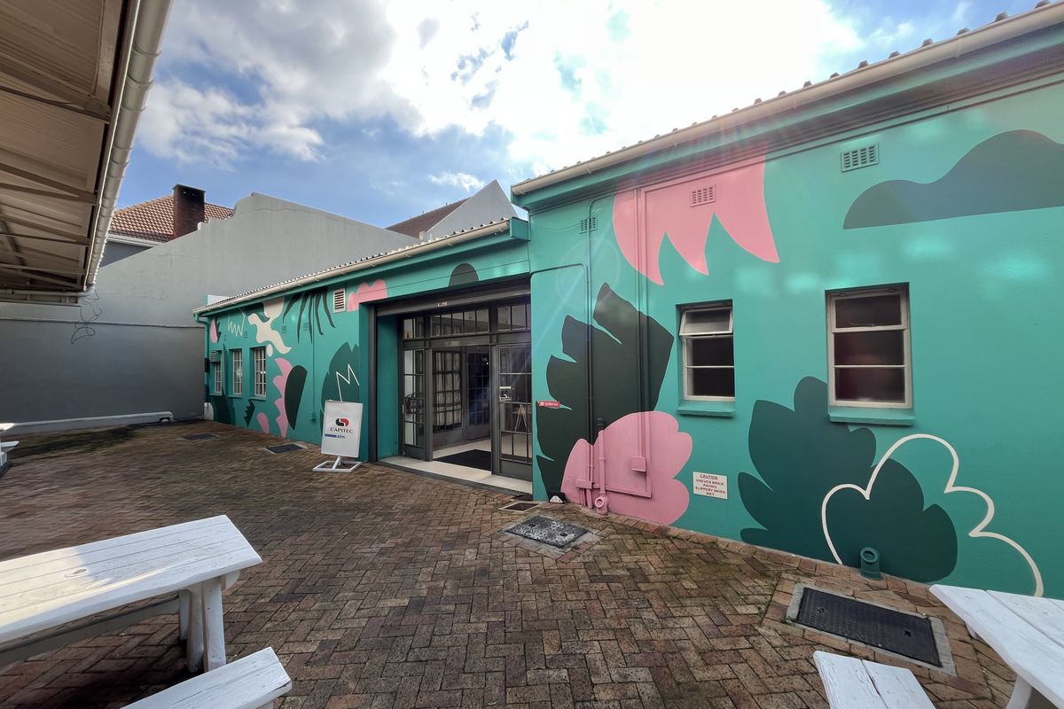 A rear exterior view of a commercial building featuring a vibrant mural, brick-paved courtyard area, and glass-paneled entrance doors.