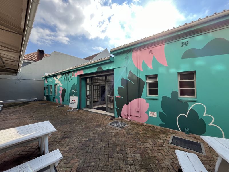 A rear exterior view of a commercial building featuring a vibrant mural, brick-paved courtyard area, and glass-paneled entrance doors.