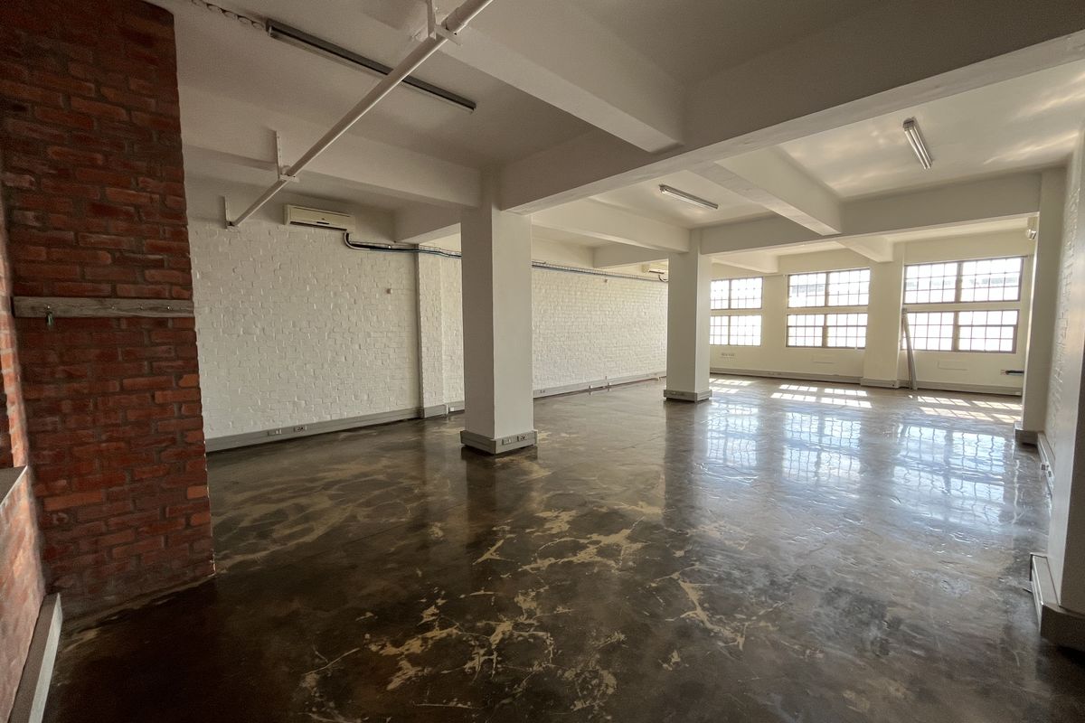 Spacious open-plan office area featuring polished concrete floors, exposed brick accents, industrial-style windows, and high ceilings with exposed structural beams.