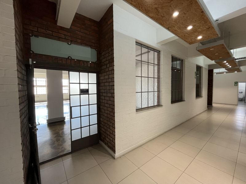 Modern industrial-style hallway featuring exposed brick walls, large steel-framed windows, tiled flooring, and unique suspended timber ceiling panels with integrated lighting.