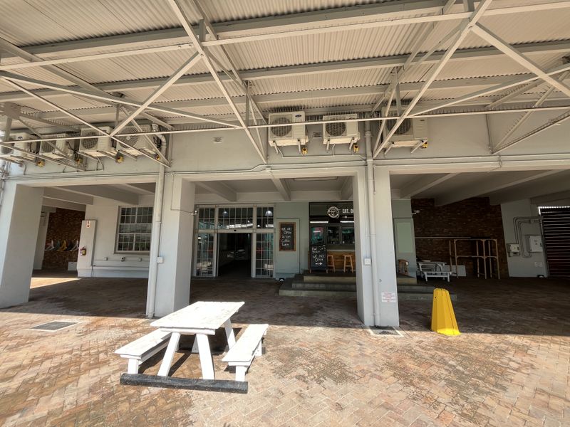 A spacious covered outdoor patio area featuring exposed steel roof trusses, brick paving, and multiple wall-mounted air conditioning units.