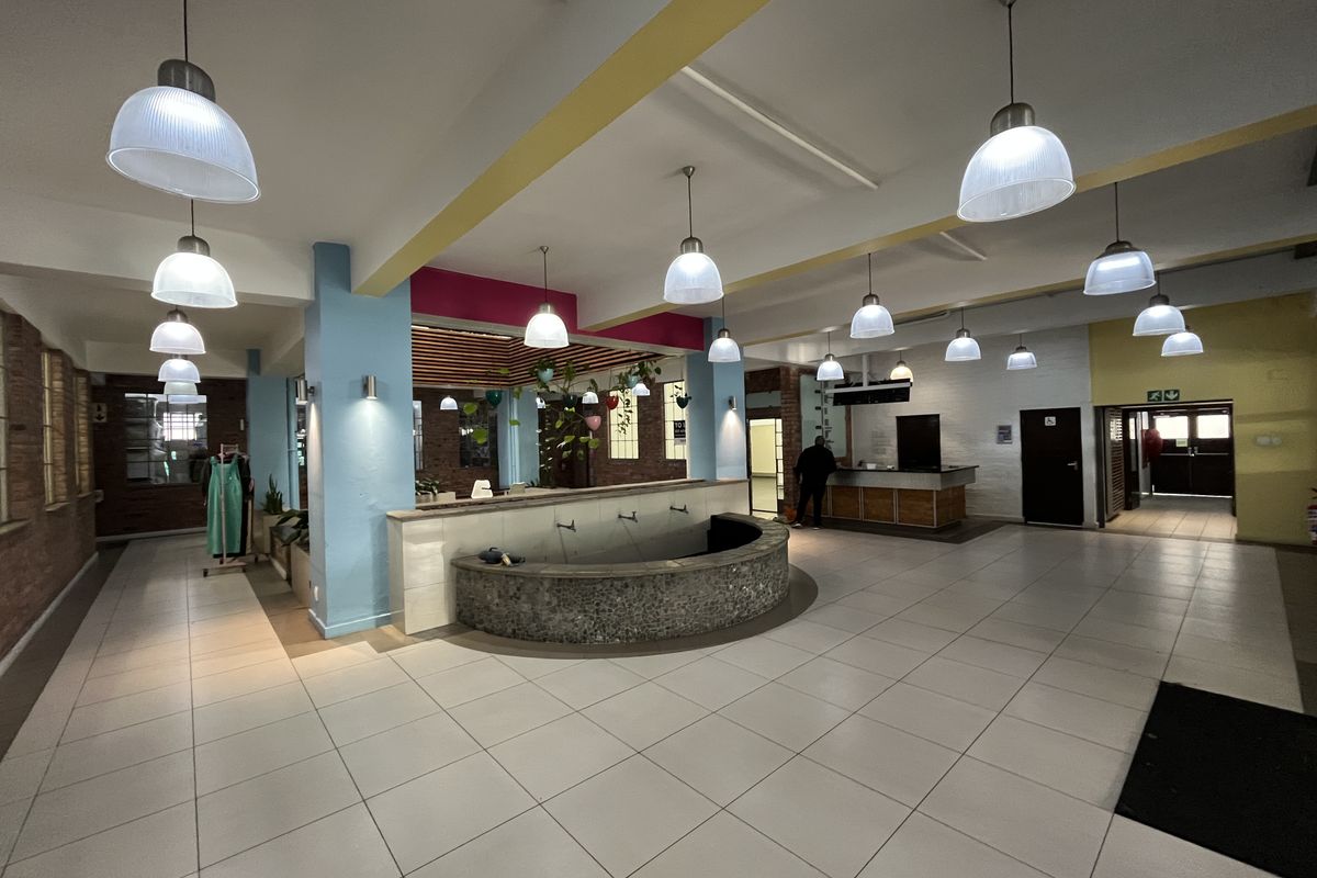 Spacious open-plan commercial interior featuring tiled flooring, multiple pendant lights, a central built-in water feature, and a reception area with exposed brick accents.
