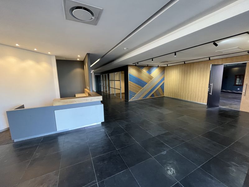 Modern office reception area featuring a built-in desk, decorative wall paneling, glass partitions, and high-quality tiled flooring with recessed and track lighting.