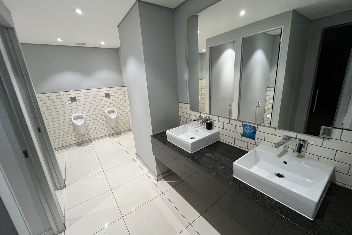 Modern office restroom featuring dual vessel sinks on a granite vanity, subway tile backsplash, and wall-mounted urinals in a clean, well-lit space.