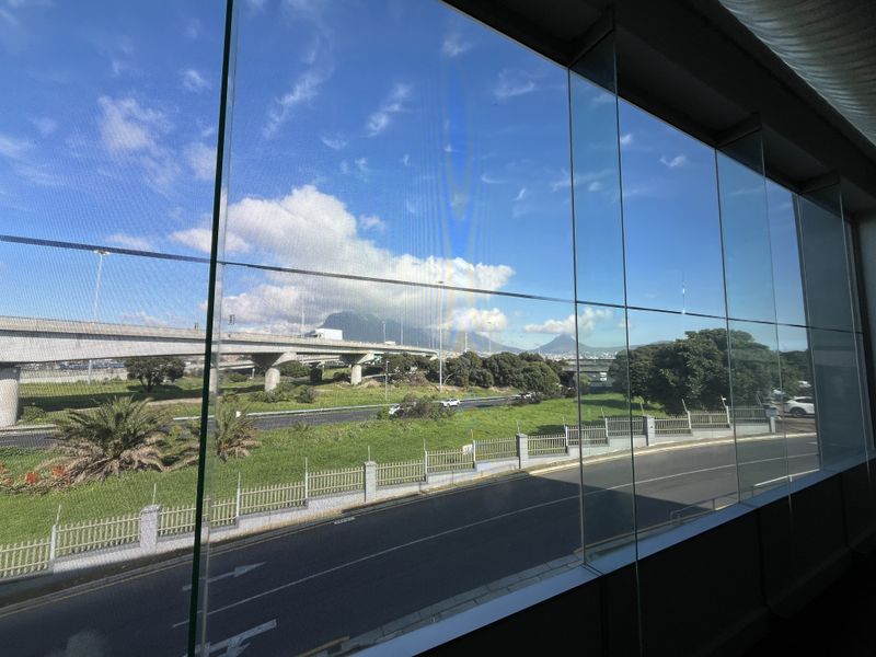 A view from an office interior looking out through a large glass curtain wall at the surrounding highway and mountain landscape.