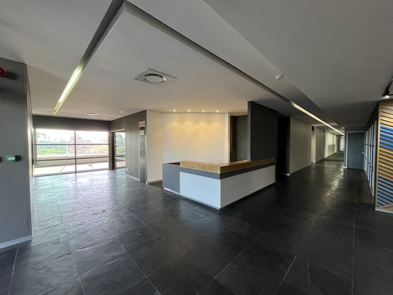 Modern office entrance area featuring a built-in reception desk, sleek dark floor tiles, and contemporary recessed ceiling lighting in a spacious, open layout.
