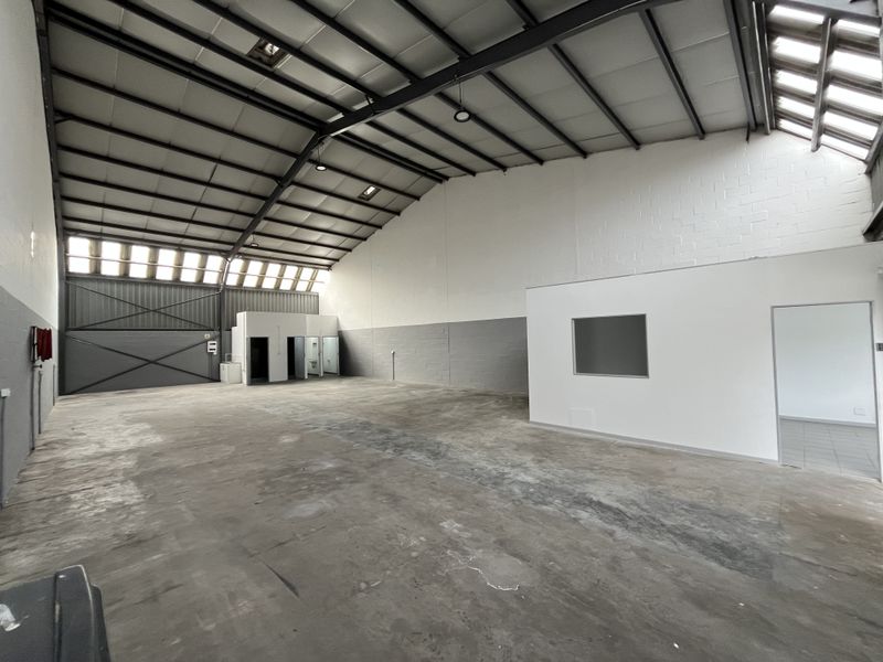 Spacious industrial warehouse unit featuring high ceilings with exposed steel trusses, concrete flooring, integrated office space, and natural light from skylights.