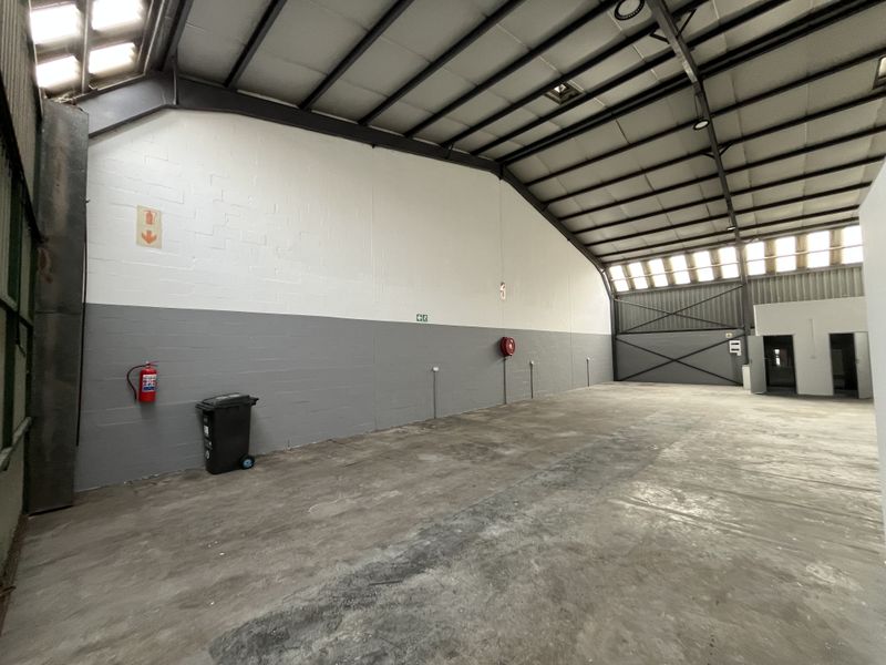 Spacious industrial warehouse unit featuring high ceilings with exposed steel trusses, concrete flooring, and essential fire safety equipment.