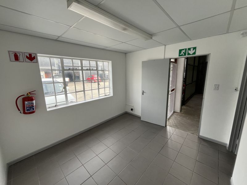 A clean, empty office space featuring tiled flooring, a suspended ceiling, and a fire extinguisher, providing a functional workspace within an industrial setting.