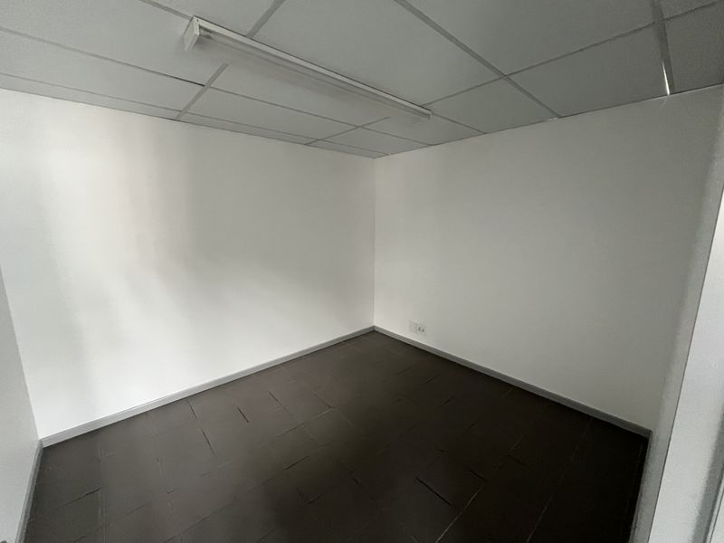 A clean, empty office space featuring a suspended ceiling, fluorescent lighting, and dark tiled flooring, suitable for a professional workspace.