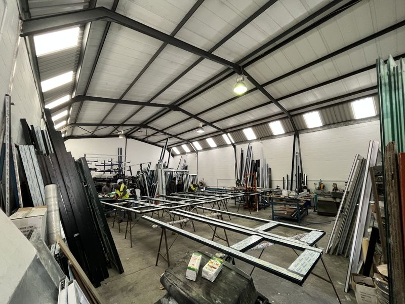 Spacious industrial workshop featuring an exposed steel portal frame, high ceilings with integrated skylights, and durable concrete flooring, suitable for manufacturing or storage operations.