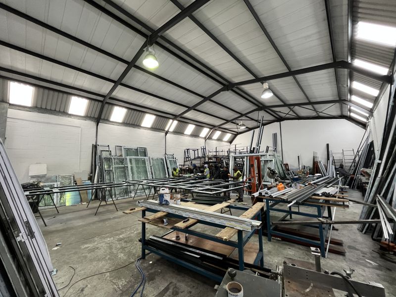Spacious industrial workshop featuring high-pitched steel truss roofing, abundant natural light from skylights, and durable concrete flooring suitable for manufacturing or fabrication operations.