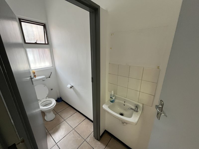 A functional bathroom featuring a toilet and a wall-mounted basin with tiled splashback and flooring, requiring minor cosmetic repairs.