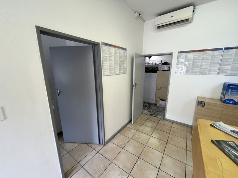 Functional office space featuring ceramic tiled flooring, a wall-mounted air conditioning unit, and access to adjacent utility or storage areas.