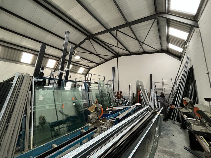 Industrial workshop space featuring high ceilings with exposed steel trusses, integrated skylights, and durable concrete flooring, currently utilized for manufacturing and storage.