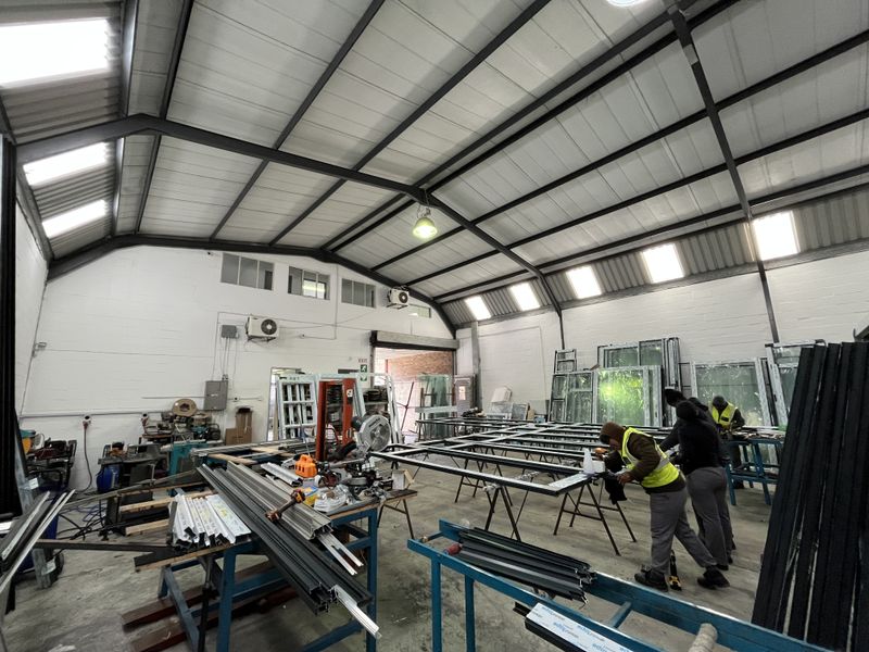 Spacious industrial workshop featuring an exposed steel portal frame, high ceilings with integrated skylights, and durable concrete flooring, currently utilized for manufacturing operations.