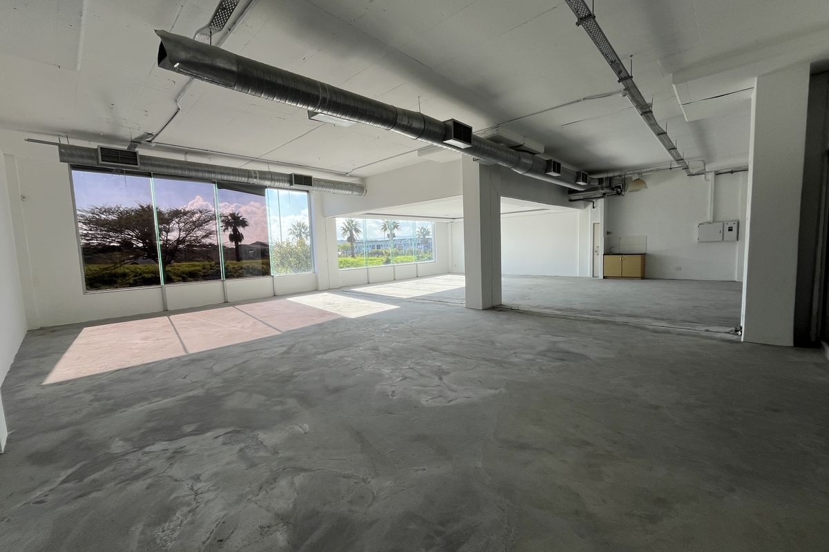Spacious open-plan commercial office area featuring exposed industrial ducting, polished concrete flooring, and expansive windows providing ample natural light.