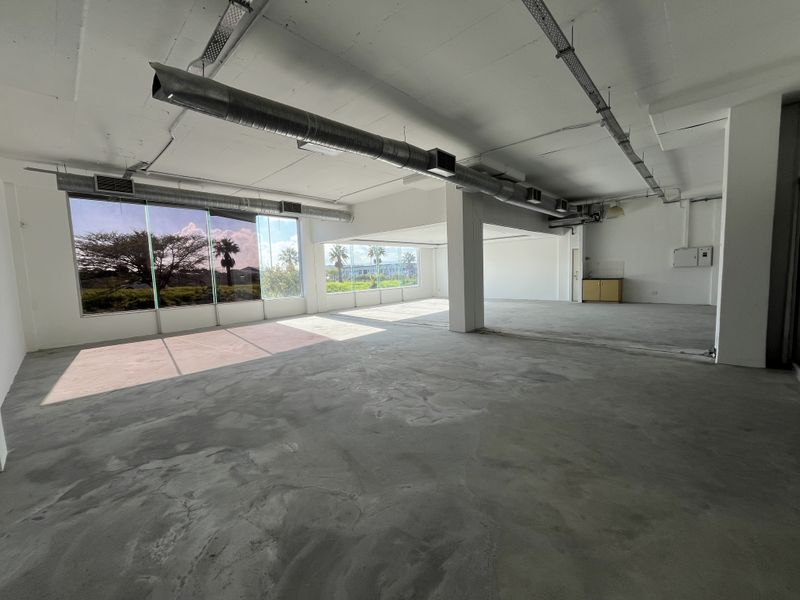 Spacious open-plan commercial office area featuring exposed industrial ducting, polished concrete flooring, and expansive windows providing ample natural light.