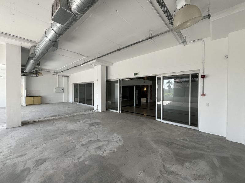 Spacious open-plan commercial area featuring exposed industrial ducting, concrete flooring, and large sliding glass doors providing natural light and access.