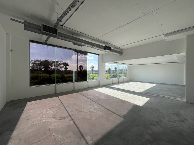 Spacious open-plan office area featuring exposed industrial ducting, polished concrete flooring, and expansive windows providing ample natural light and exterior views.