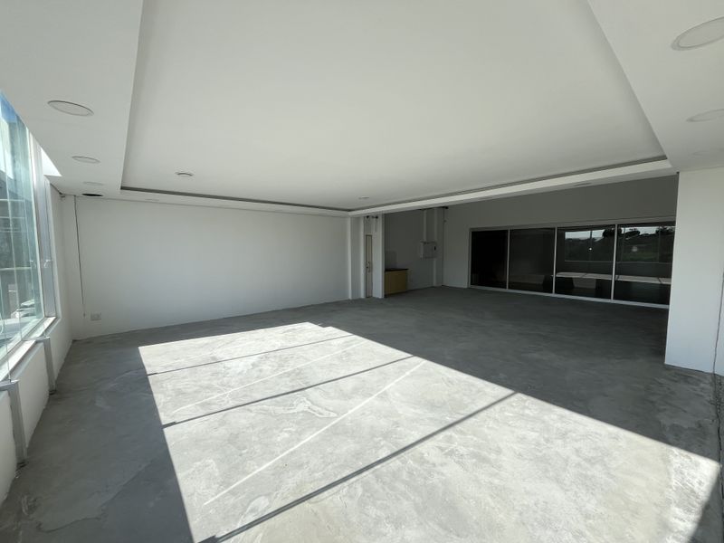 Spacious open-plan commercial area featuring large windows, sliding glass doors, recessed ceiling lighting, and unfinished concrete flooring, offering a versatile blank canvas.