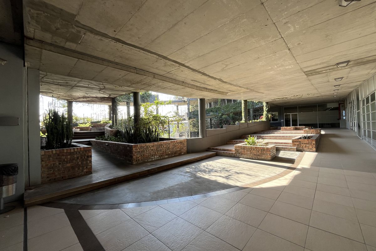 A spacious covered outdoor terrace featuring exposed concrete ceilings, tiered brick planter boxes, and a combination of tiled and timber deck flooring.