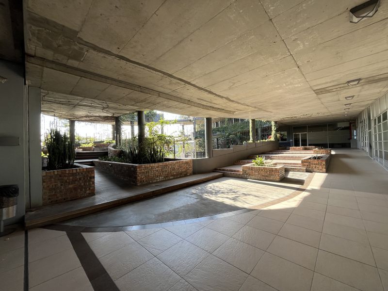 A spacious covered outdoor terrace featuring exposed concrete ceilings, tiered brick planter boxes, and a combination of tiled and timber deck flooring.