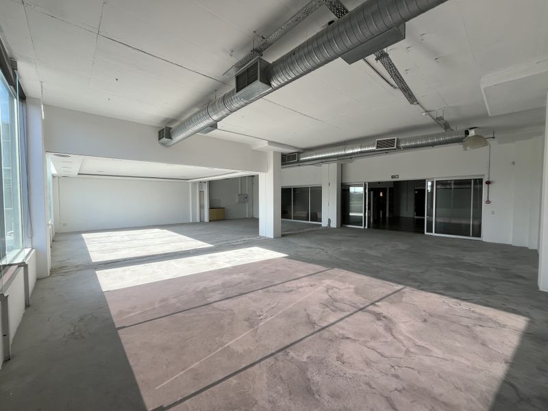 Spacious open-plan commercial office area featuring industrial-style exposed ductwork, polished concrete flooring, and large windows providing ample natural light.