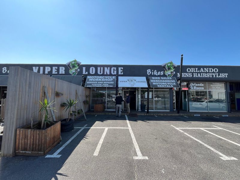 Front exterior view of a commercial property featuring multiple business storefronts, including a motorcycle workshop and lounge, with dedicated paved parking.
