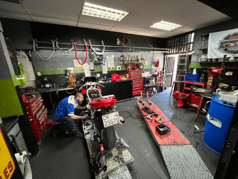 A functional workshop garage space featuring industrial lighting, metal workbenches, and durable diamond plate flooring, currently utilized for motorcycle maintenance.