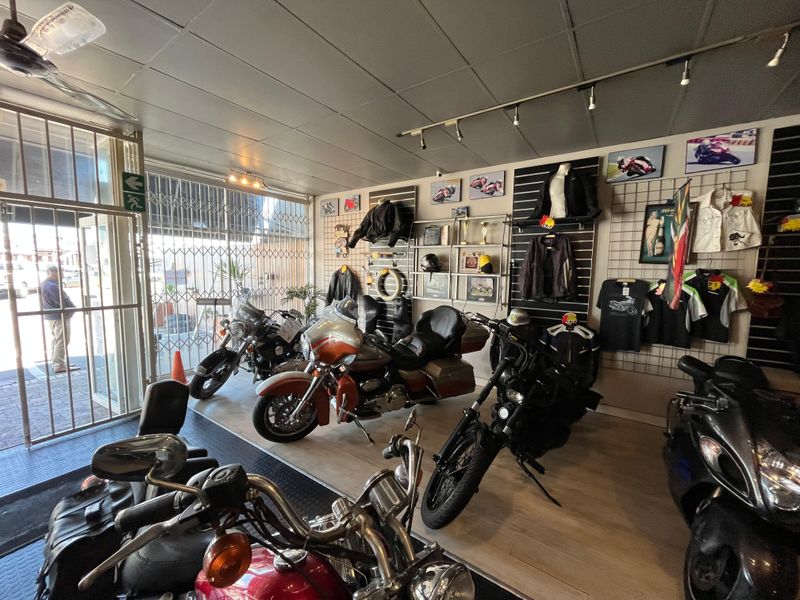 A commercial showroom space featuring slatwall display systems, track lighting, and a secure metal entrance gate, currently utilized for motorcycle retail.
