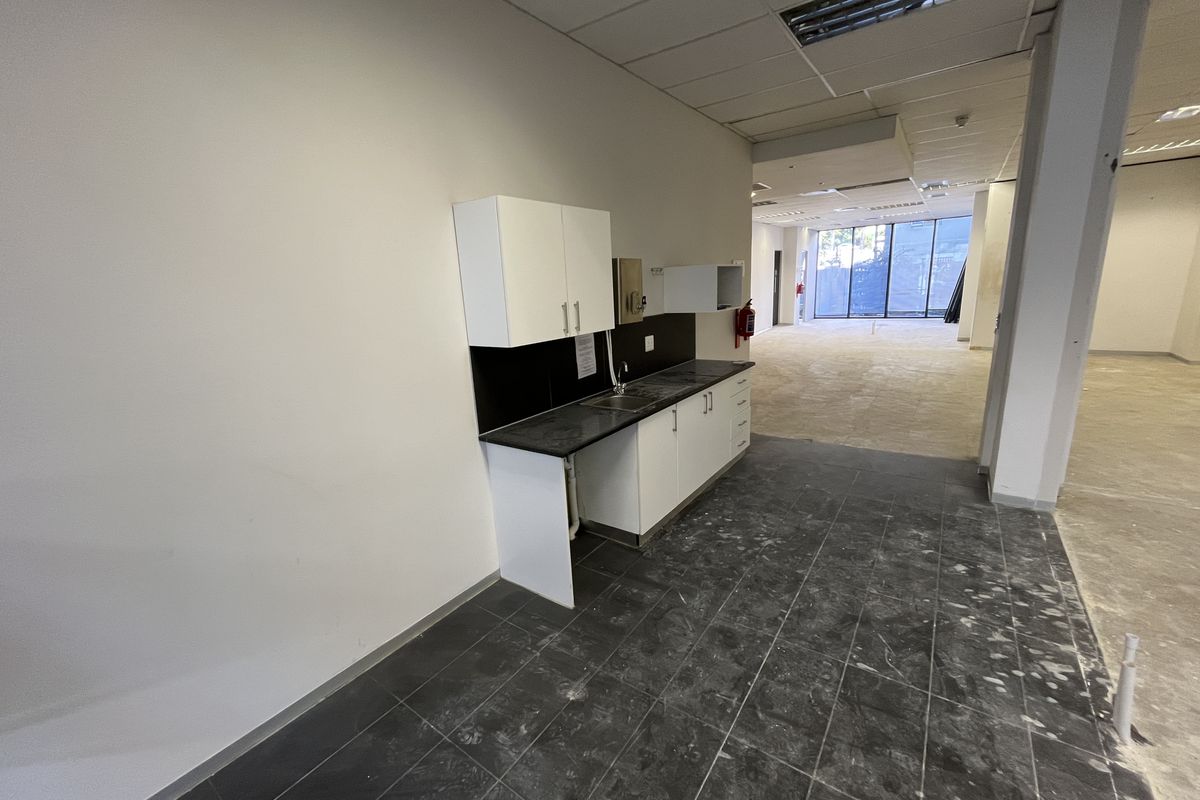 A compact office kitchenette featuring built-in cabinetry, a sink, and dark tiled flooring, situated within an open-plan office space.