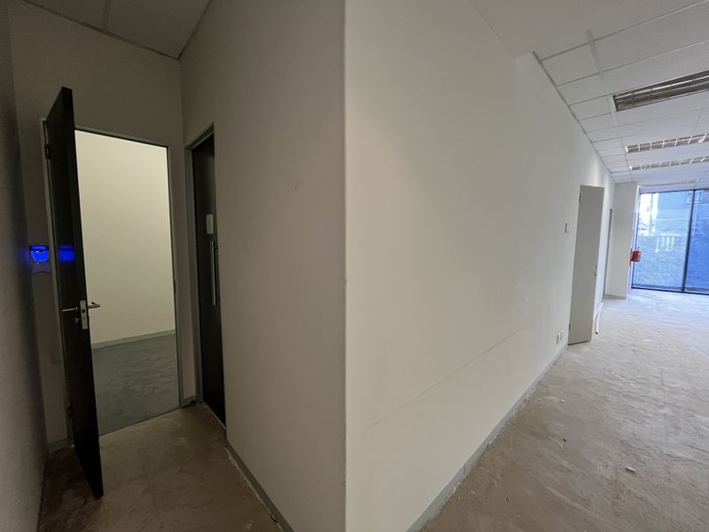 An empty office space featuring a suspended ceiling, recessed lighting, and access to multiple rooms, currently requiring flooring and wall finishing.