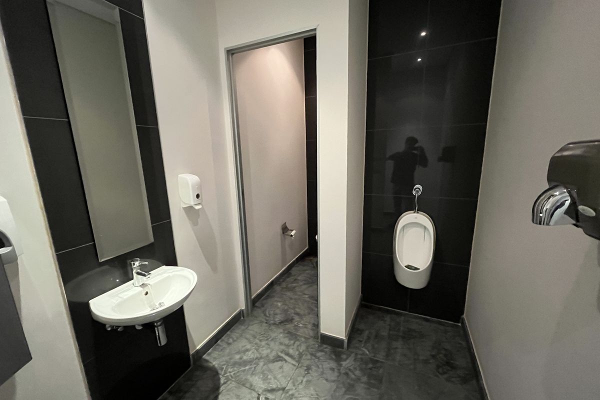 Modern office bathroom featuring a wall-mounted basin, a wall-mounted urinal, dark tiled feature walls, and contemporary fixtures.