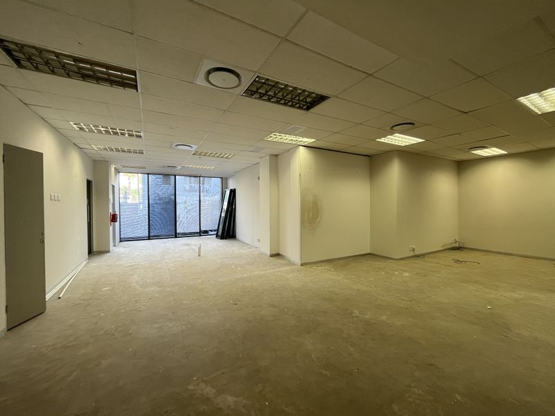 An empty, open-plan office space featuring a suspended ceiling, recessed lighting, and large windows, currently requiring floor and wall finishing.