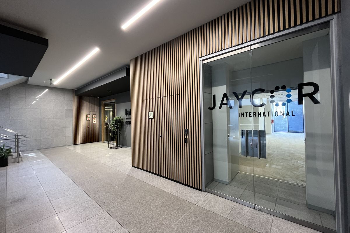Modern office entrance featuring contemporary timber slat wall paneling, glass entry doors, and clean tiled flooring with recessed linear lighting.