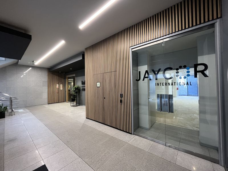 Modern office entrance featuring contemporary timber slat wall paneling, glass entry doors, and clean tiled flooring with recessed linear lighting.