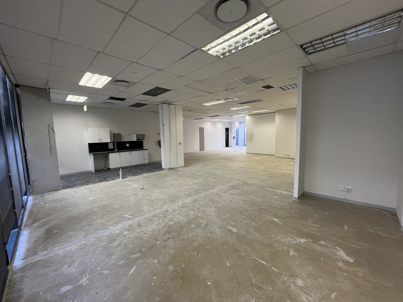 An open-plan office space featuring a kitchenette, suspended ceiling with recessed lighting, and unfinished concrete flooring, ready for tenant fit-out.