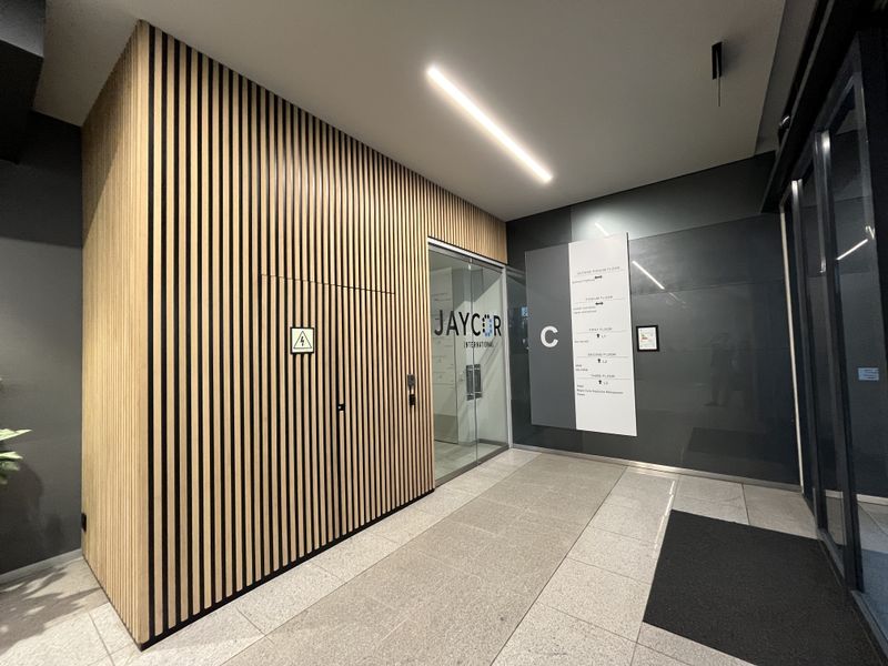 Modern office building entrance lobby featuring contemporary slatted timber wall paneling, glass entry doors, and clear directional signage.