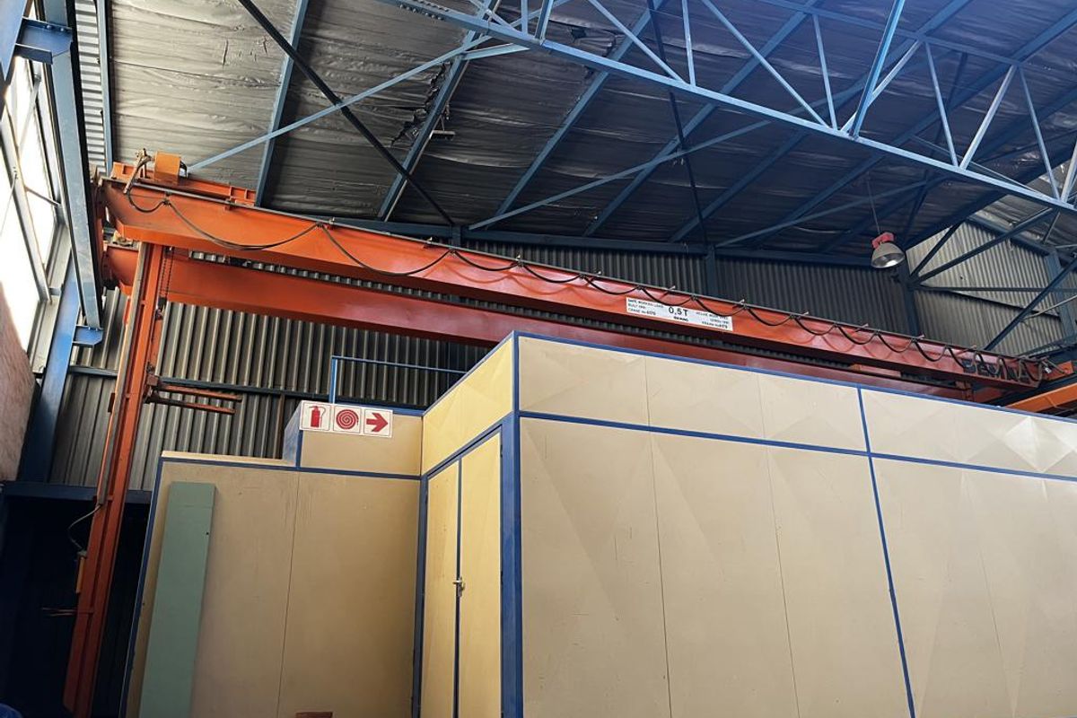 Industrial warehouse interior featuring a 0.5-ton overhead crane, exposed steel roof trusses, and a partitioned office structure.