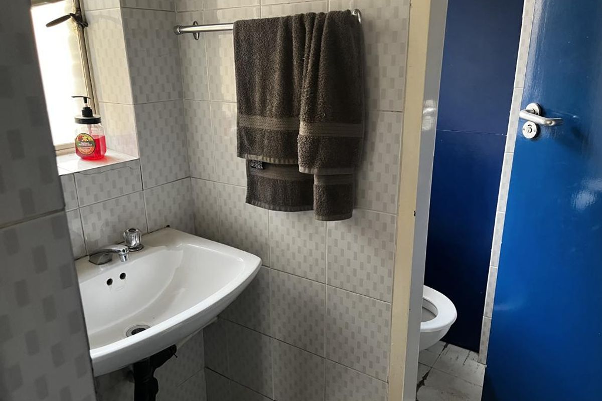 A compact bathroom featuring a wall-mounted basin, tiled walls, and a separate toilet area with a blue door.
